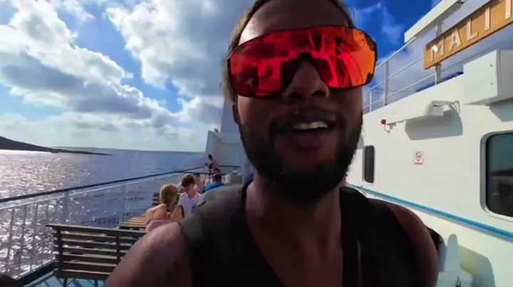 Ray smiling in red sunglasses on a ferry deck under a blue sky