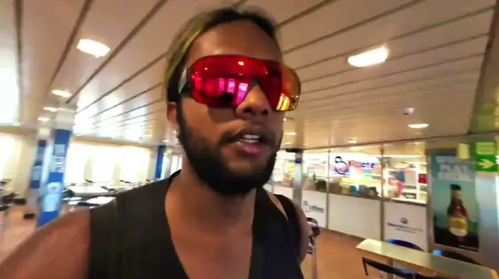 Ray in red sunglasses talking to the camera inside a ferry cafe
