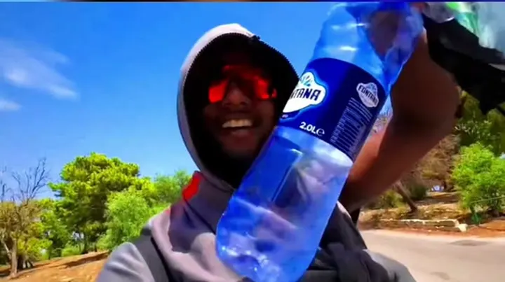 Ray laughing in a hoodie, holding up a water bottle in the sun