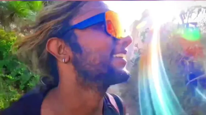 Ray laughing in blue sunglasses with a rainbow lens flare