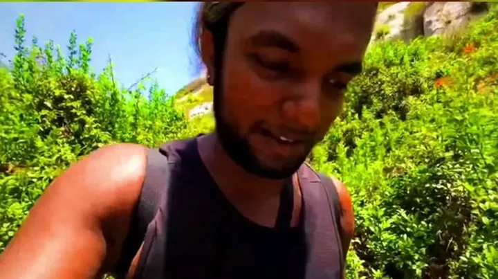 Ray smiling down at the camera among green bushes